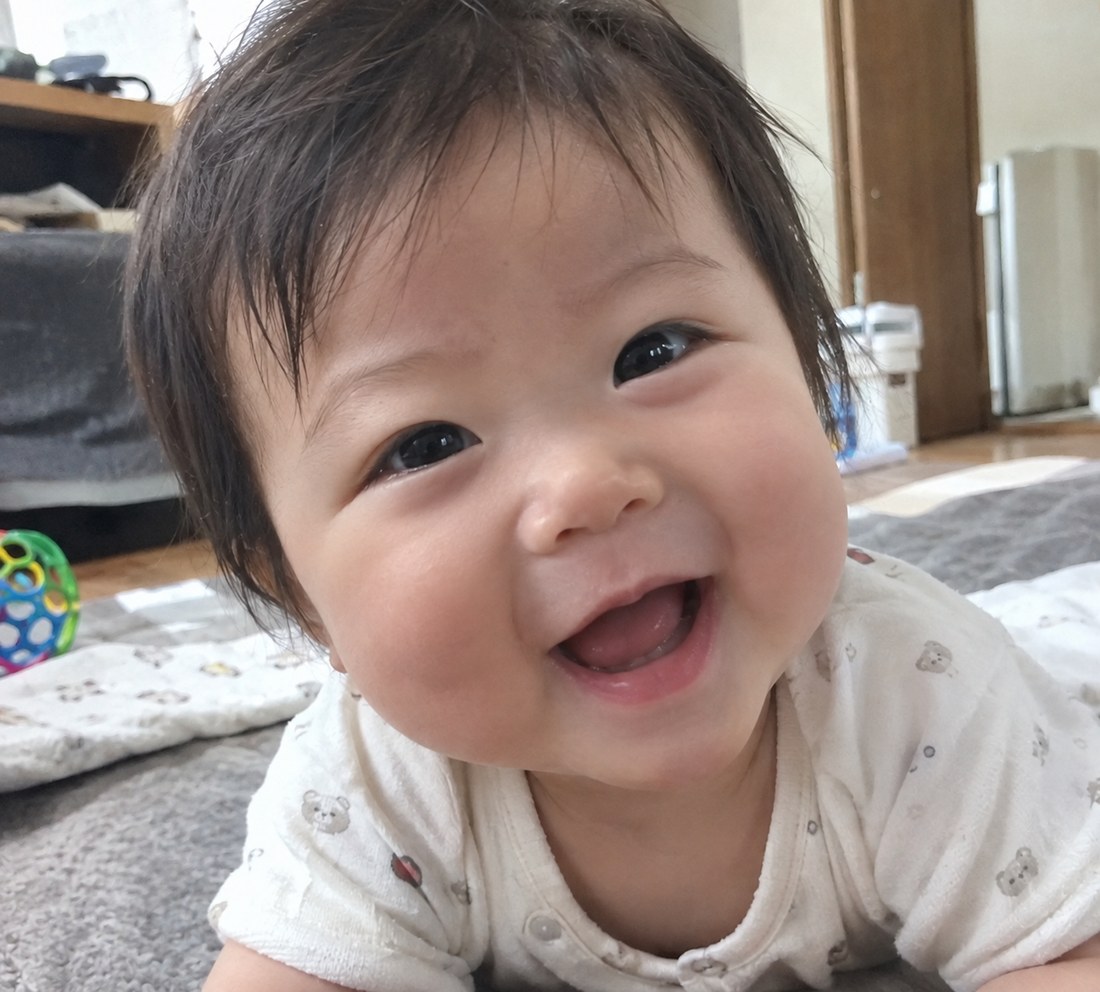 床にうつ伏せになって笑っている赤ちゃんの写真